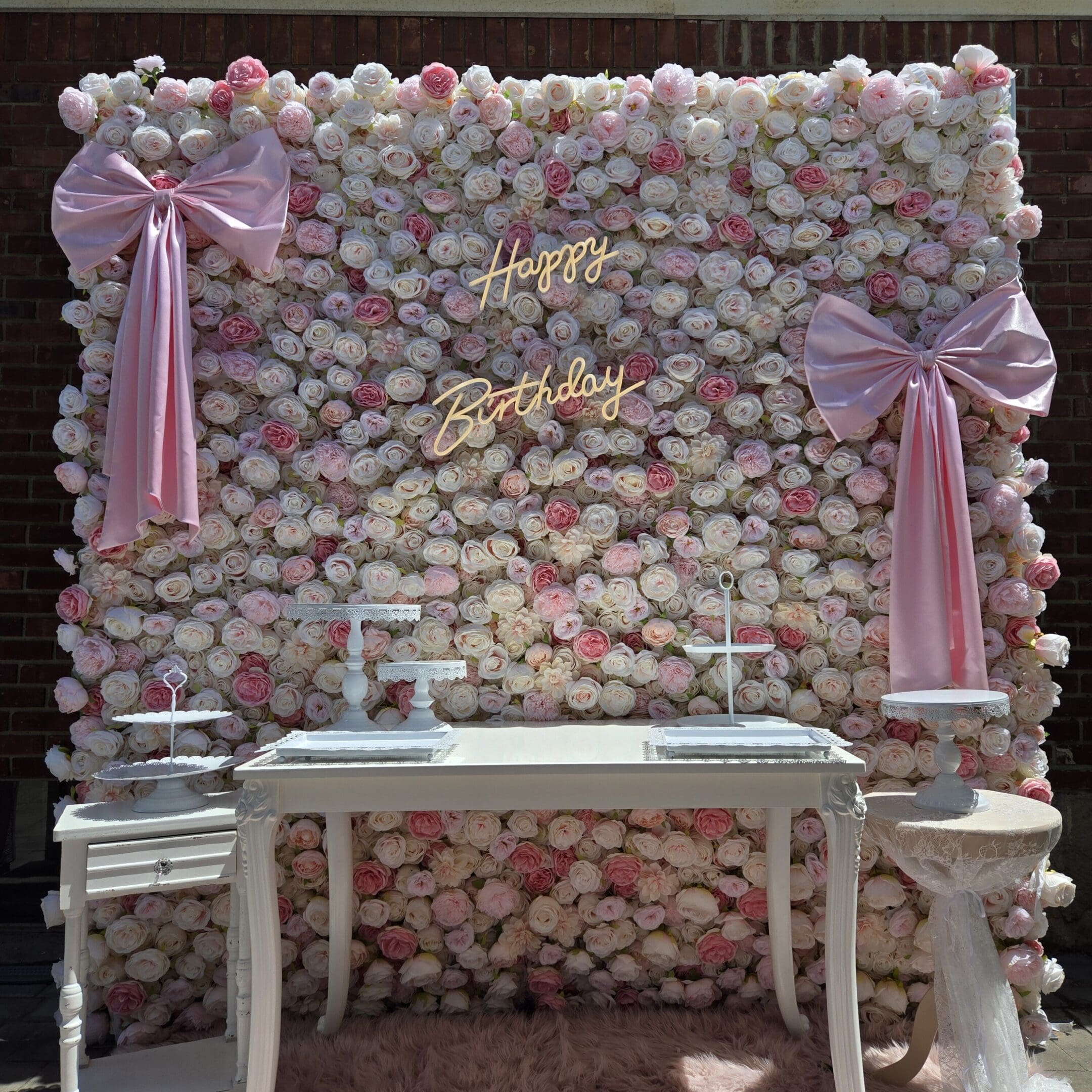 Elegant floral backdrop with white table and pink ribbons for a special event.